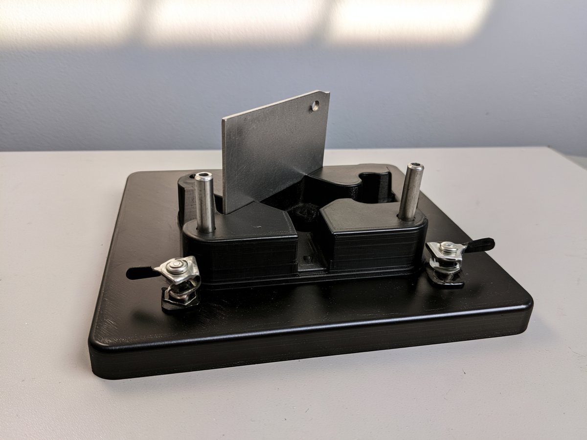 Black plastic assembly fixture holding a steel bracket with toggle clamps