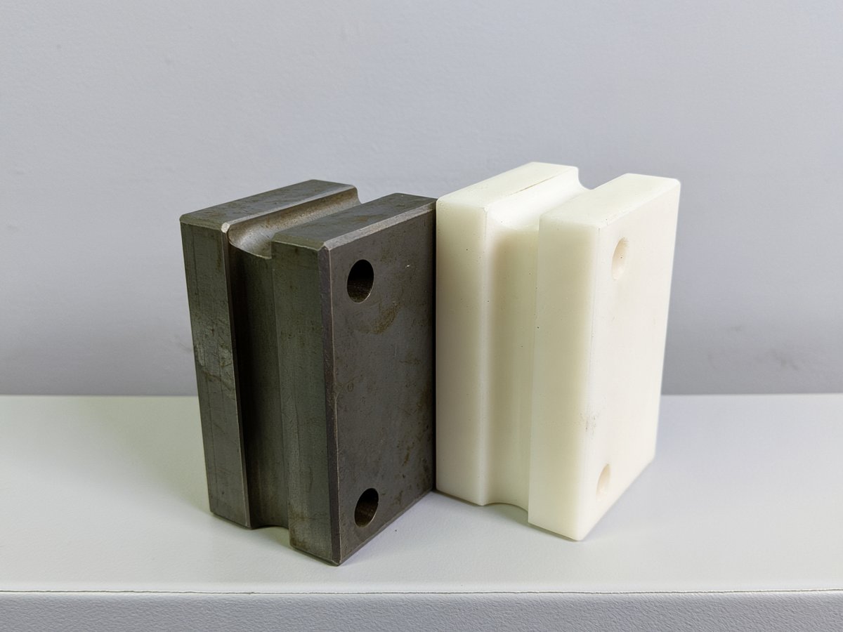 Steel guide block next to an identical white engineering plastic replacement